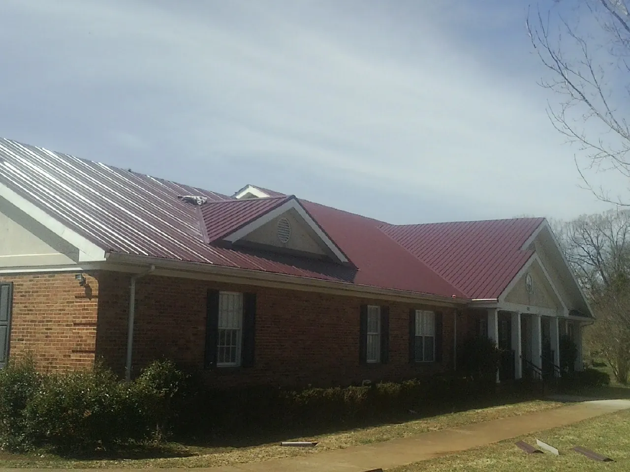 Red metal roof with gabled entries on a long brick building, from a Hail Damage Roof Repair job in Momence