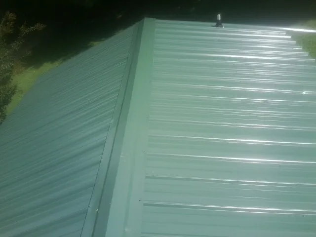 New green metal panels meeting at the ridge of a roof — Flat Roof Repair work by our crew in Momence