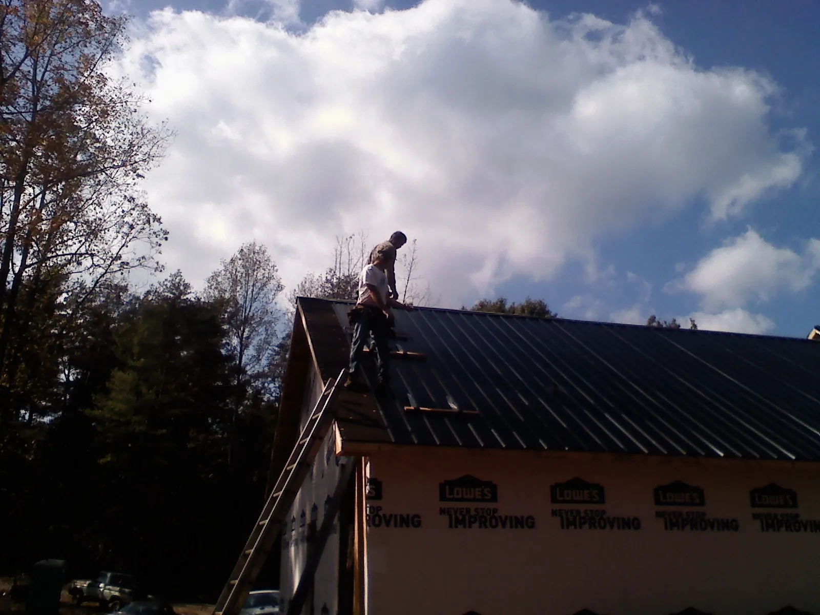 Roofer fastening dark metal panels high against a cloudy sky, from a Roof Inspection job in Momence