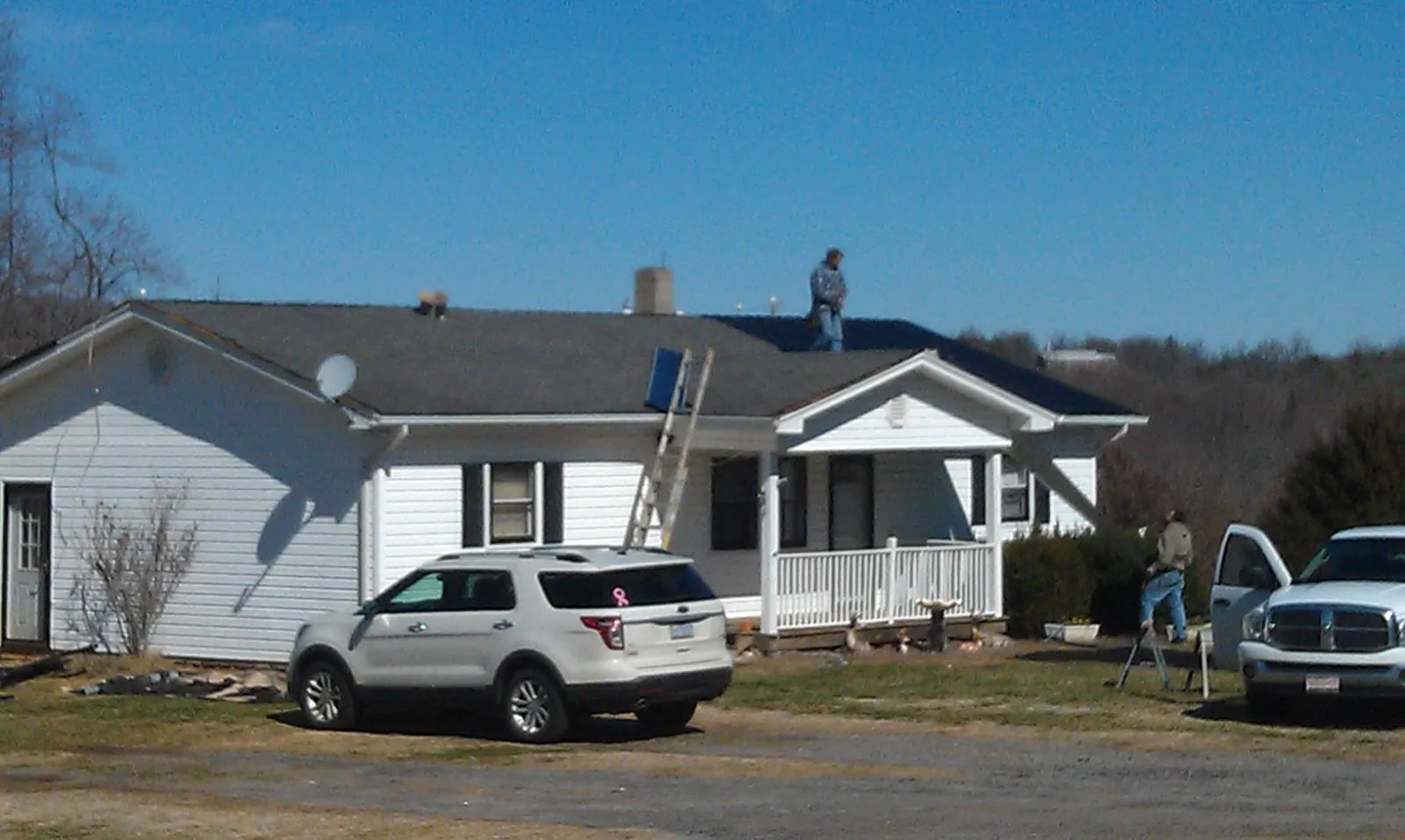 Roofers stripping shingles from a white ranch house roof in Momence