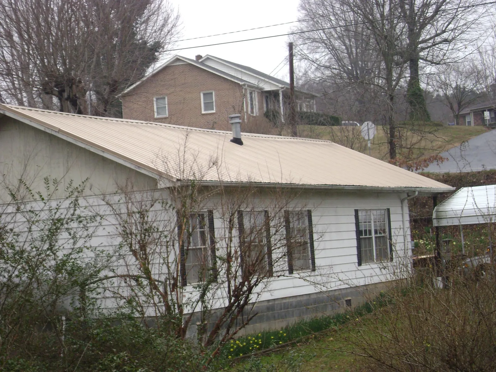 Tan metal roof on a white sided house set into a hillside — Commercial Roofing by Roofing Brothers in Momence