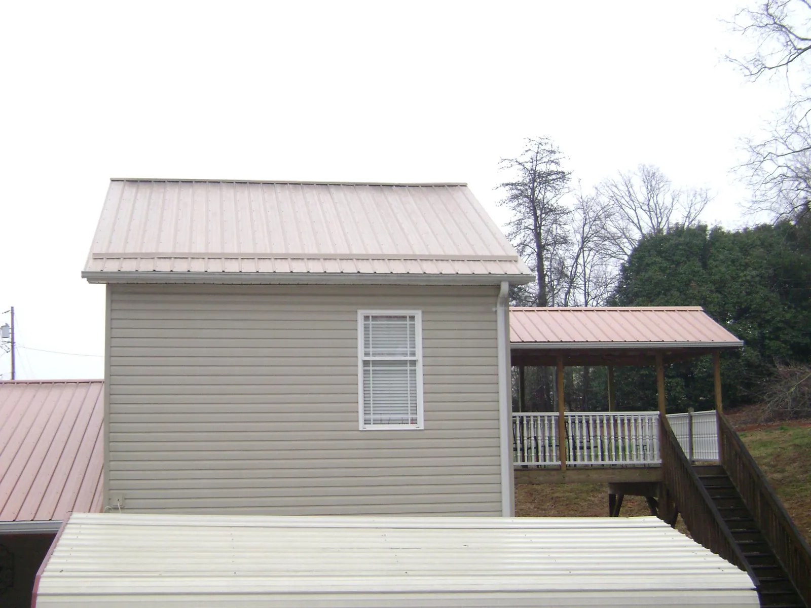 Tan metal roofs on a two story addition and attached porch, from a Roof Replacement job in Momence